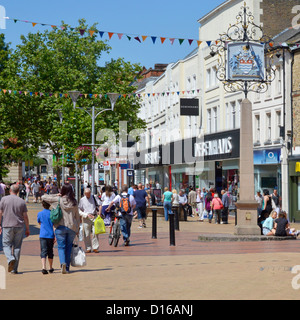 Shop front & shoppers busy pedestrianised high street shopping scene around Chelmsford City coat of arms sign on blue sky day summer day Essex UK Stock Photo