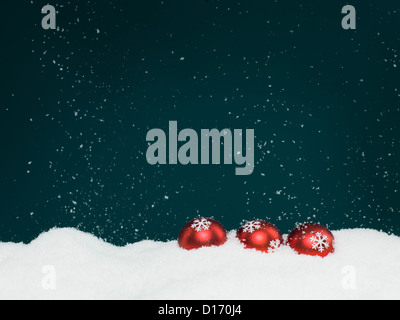 closeup of three red colored christmas globes decorated with glittery snowflakes surrounded with snow, on blue background with falling snowflakes Stock Photo