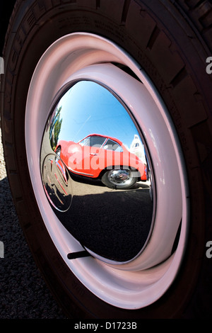 The reflection of a red classic car in a shiny chrome hubcap. Stock Photo