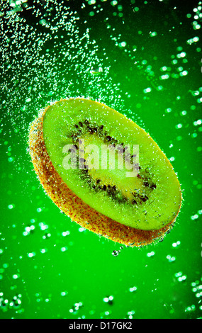 Fresh kiwi falls in water on a green background Stock Photo