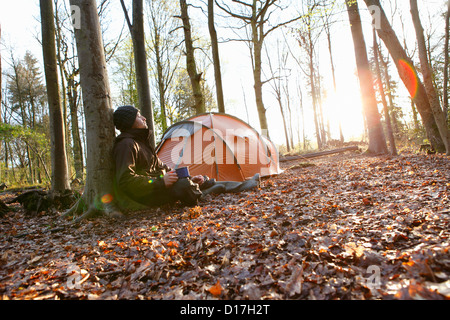 Man drinking coffee by tent in forest Stock Photo