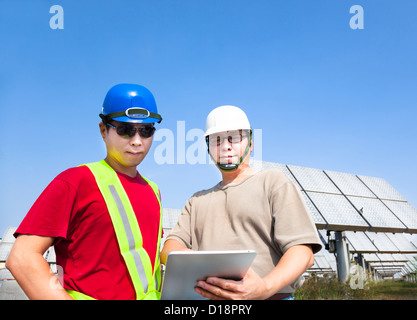 two contractors holding tablet pc and standing before solar panel tracking system Stock Photo