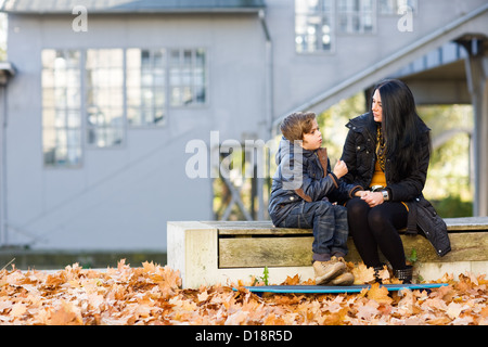 Mother and son sitting on bench and talking in front of abandoned railroad station Stock Photo