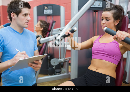 Trainer noting progress of woman using weights machine Stock Photo