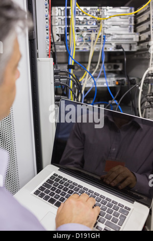 Man sitting with a laptop in front of a server Stock Photo