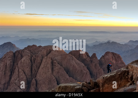 An individual watches sunrise from the edge of a cliff on top of Mount Sinai in the Sinai desert Stock Photo