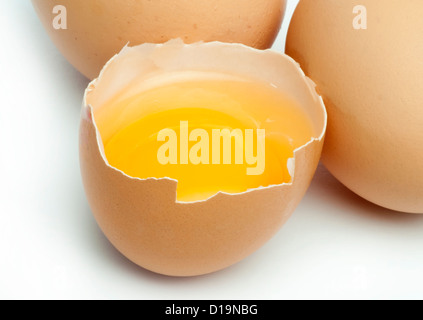 Tree whole eggs and another broken in half raw egg and yolk inside. Placed on white background. Stock Photo