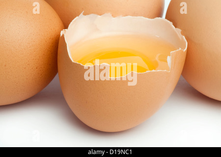 Tree whole eggs and another broken in half raw egg and yolk inside. Placed on white background. Stock Photo