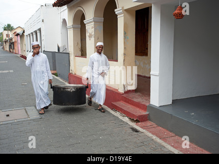 Two Muslim men carry a large cooking pot down a street in Galle Fort Sri Lanka Stock Photo