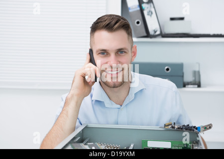 Portrait of smiling computer engineer on call in front of open cpu Stock Photo