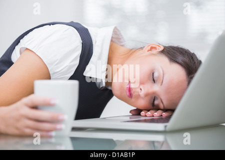 Business woman with coffee cup resting head on laptop at office Stock Photo