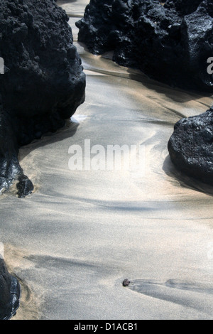 Black and golden sand mixing between lava rocks on Maui Island beach, Hawaii, USA Stock Photo