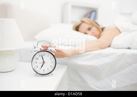 Irritated young woman in bed extending hand to alarm clock Stock Photo