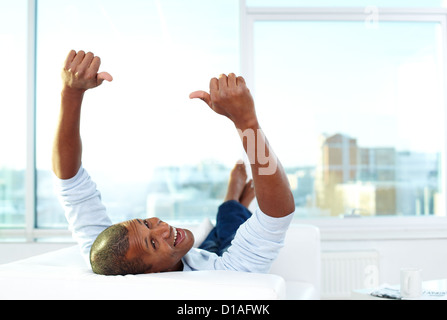 Image of young African man lying on sofa with thumbs up and looking at camera Stock Photo