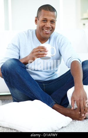 Image of young African man with cup sitting on the floor and looking at camera Stock Photo