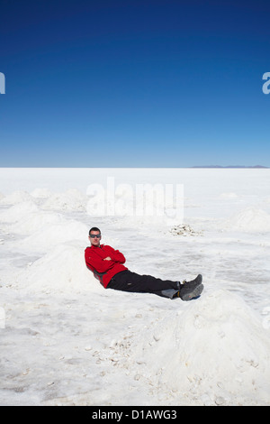 Man sitting next to piles of salt on Salar de Uyuni (Salt Flats of Uyuni), Potosi Department, Bolivia Stock Photo