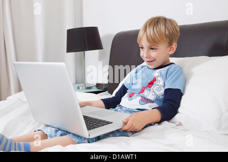 Smiling Caucasian boy using laptop computer in bed Stock Photo