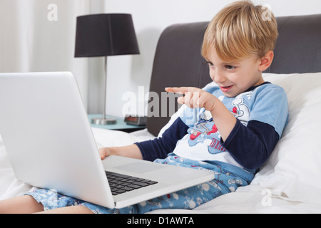 Playful Caucasian boy using laptop computer in bed Stock Photo