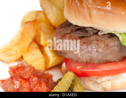 Simple home made basic hamburger with tomato slices, lettuce and onion in a white bread bun with chips and pickles. Stock Photo