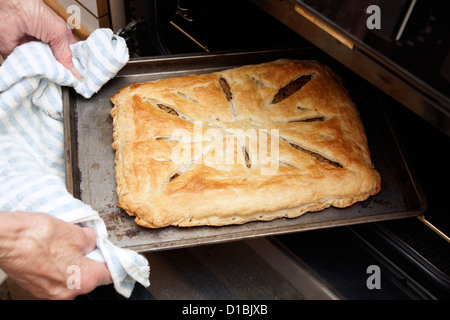 Elderly woman home baking taking a savoury pastry pie out of the oven Stock Photo