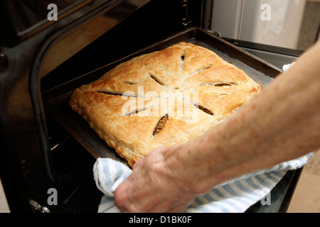 Elderly woman home baking taking a savoury pastry pie out of the oven Stock Photo