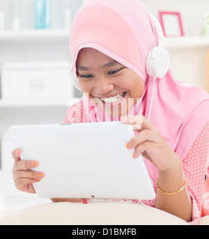 Southeast Asian teenager listen mp3 headphone at home. Muslim teen girl living lifestyle. Stock Photo