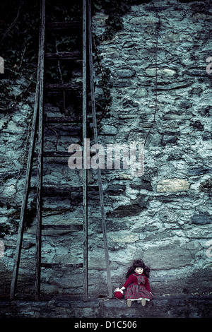 an old doll sitting on a wall next to an old wooden ladder Stock Photo