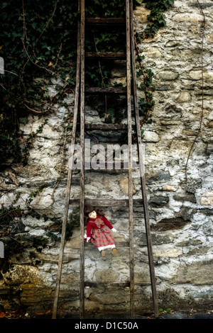 an old doll sitting on an old wooden ladder Stock Photo