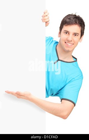 A smiling handsome male gesturing behind a blank panel isolated against white background Stock Photo