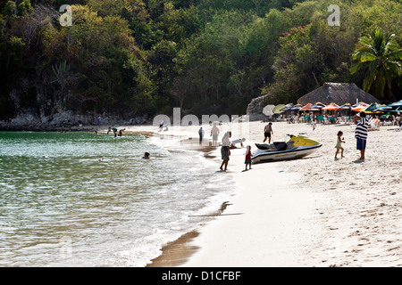 afternoon light silhouettes people enjoying sandy beach & clear translucent water against jungle background of Playa Santa Cruz Stock Photo