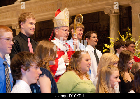 Priest wearing red vestments surrounded by teenagers during confirmation Mass Basilica of 'St Mary' Minneapolis Minnesota MN USA Stock Photo