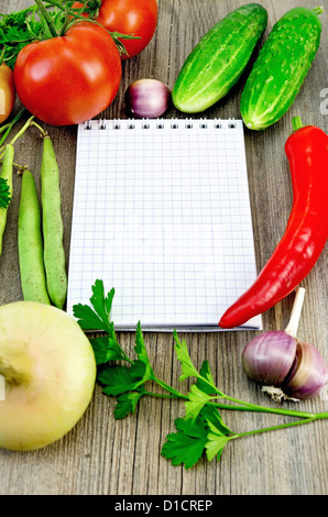 Small notepad, red tomatoes, pod red pepper, parsley, garlic, onion, two cucumbers, green bean pods on an old wooden board Stock Photo
