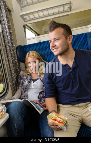 Man looking out train window woman magazine sandwich reading smiling Stock Photo