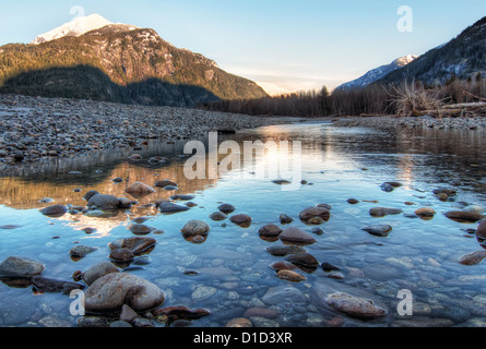 Clear river with rocks leads towards mountains lit by sunset Stock Photo