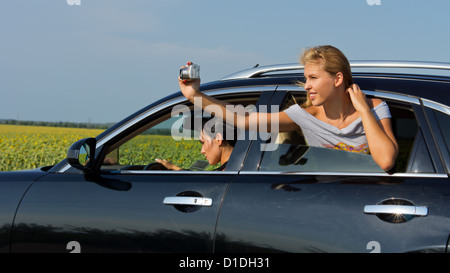 Beautiful young blonde woman passenger leaning out of car window taking a photograph of herself Stock Photo
