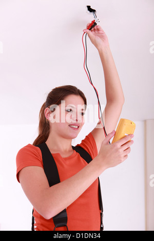 Woman using a voltmeter on ceiling electrics Stock Photo