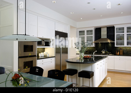 KITCHEN horizontal with frosted glass top table in foreground kitchen island dark green / black granite counters stainless Stock Photo