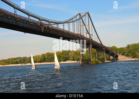 Two small vessel ships under a big metal bridge and beach on background. Kiev. Ukraine. Stock Photo