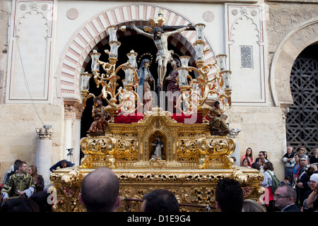 Jesus Christ on the Cross with Virgin Mary and Mary Magdalene on a gilded platform in procession during Holy Week in Cordoba. Stock Photo