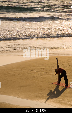 Vertical portrait of a lady practicing yoga on the beach at sunset in Varkala, Kerala. Stock Photo