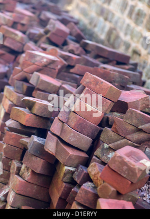 Old hand made bricks in pile stacked against stone wall Stock Photo