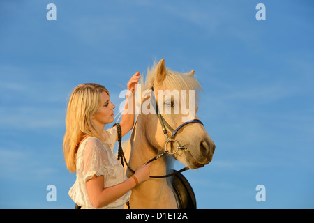 Young woman in white dress with horse under blue sky Stock Photo