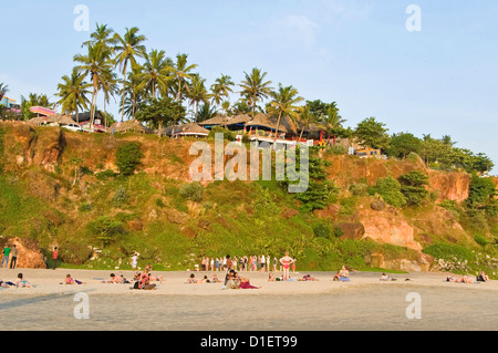 Horizontal view of people sitting relaxing on the beach with a yoga class being held in the background at Varkala, Kerala. Stock Photo