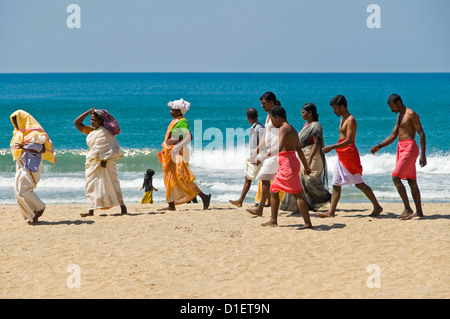 Horizontal portrait of a group of Indians walking along the beach after performing puja (prayers) at Varkala, Kerala. Stock Photo