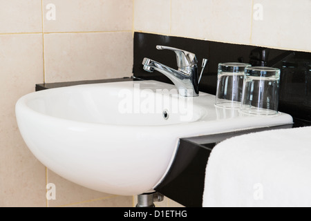 Ceramic hand wash basin in a hotel with chrome water mixer tap, white towel and two glasses Stock Photo