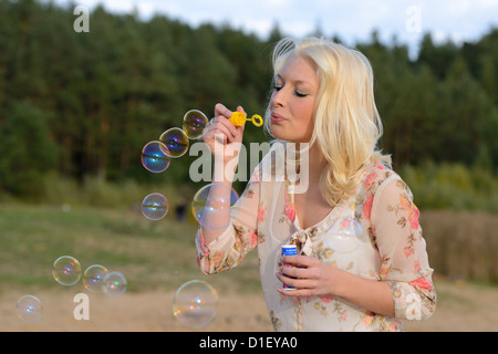 Happy young blond woman blowing soap bubbles outdoors Stock Photo