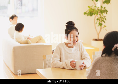 Mother and daughter having a cup of tea at the dining table with father and daughter on the sofa in the background Stock Photo