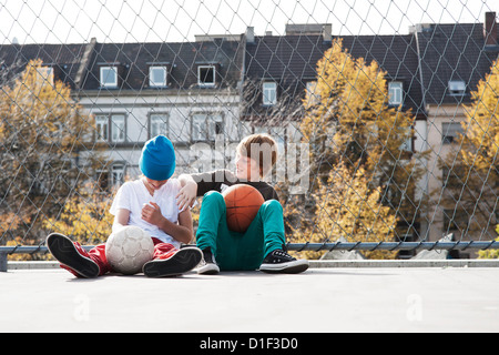 Two boys sitting on sportsground with balls Stock Photo
