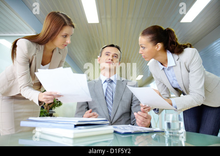 Inspirated boss sitting at workplace surrounded by two secretaries Stock Photo