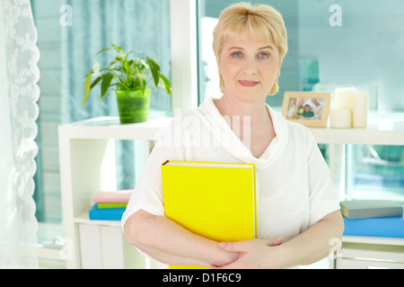 Portrait of happy mature woman with book at home Stock Photo
